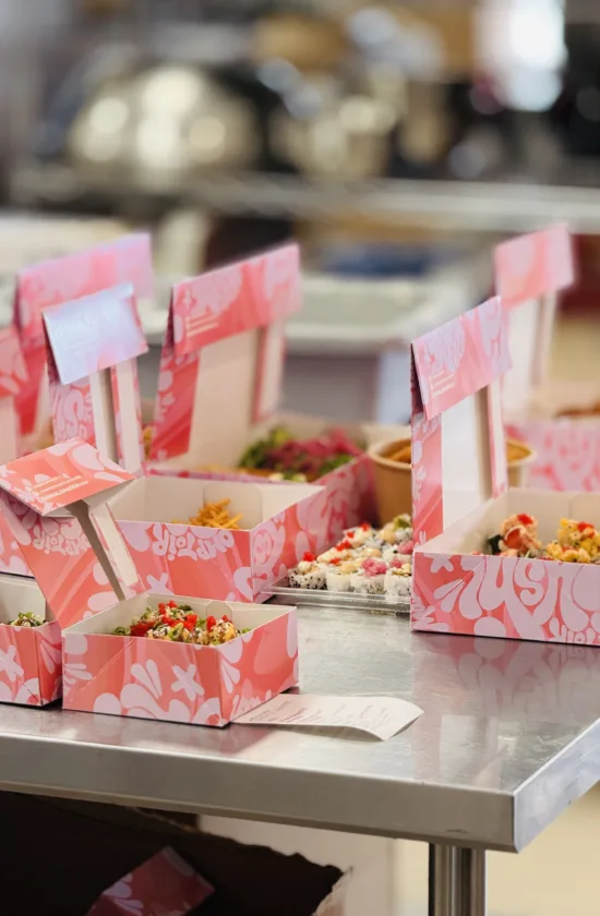 Boîtes roses Sushi à la maison remplies de bouchées colorées, prêtes à être livrées ou ramassées sur un comptoir en inox