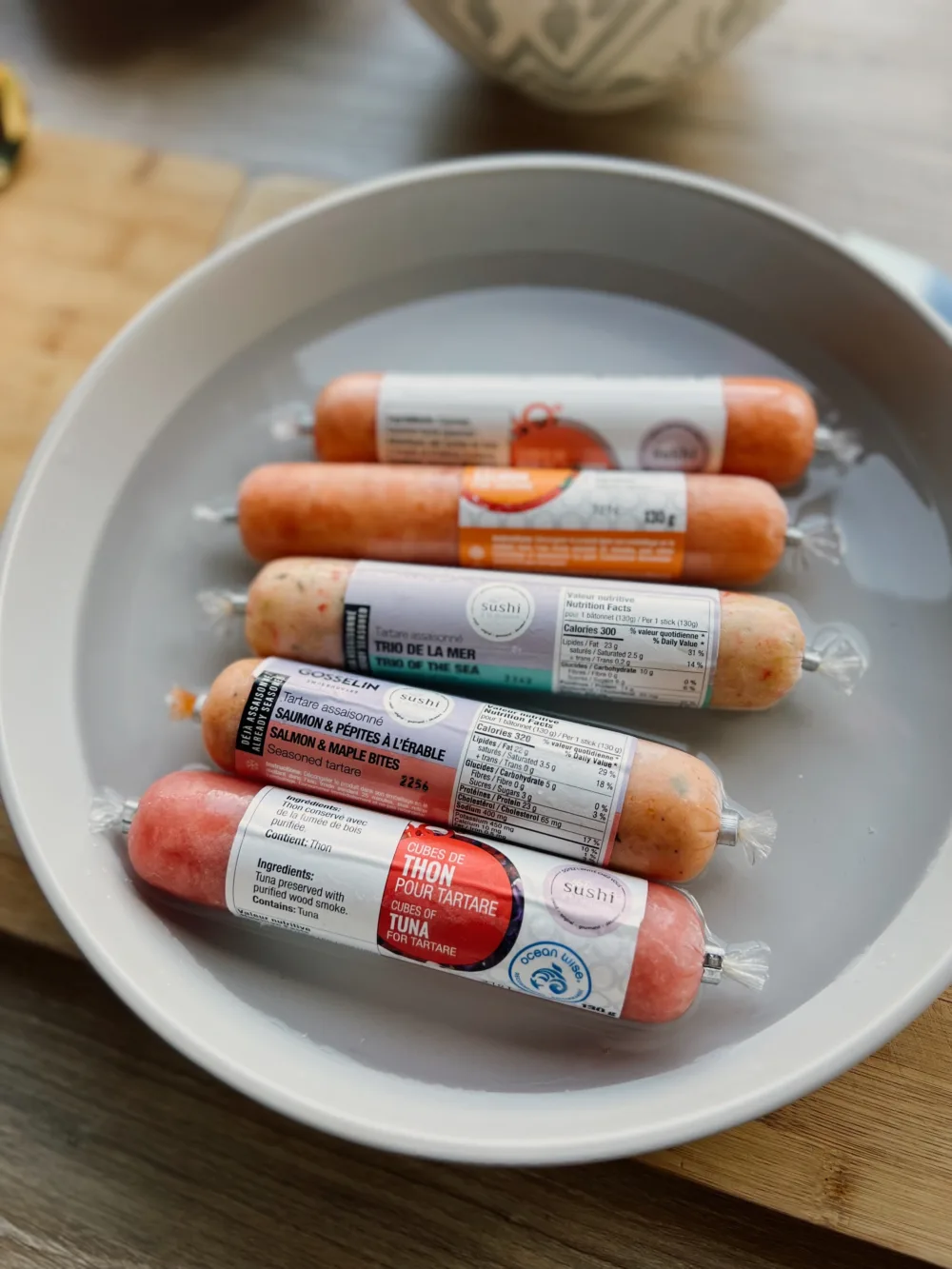 Cinq tubes de tartares Sushi à la maison présentés dans une assiette d’eau, incluant les cubes de thon pour tartare, le saumon à l’érable et le trio de la mer.