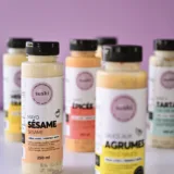Bouteilles de sauces Sushi à la maison, dont la mayo sésame, mayo épicée et sauce aux agrumes, sur fond lilas.