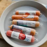 Cinq tubes de tartares Sushi à la maison présentés dans une assiette d’eau, incluant les cubes de thon pour tartare, le saumon à l’érable et le trio de la mer.